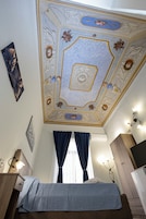 Un dormitorio con cama, mesita de noche, cómoda, televisión y techo con molduras decorativas.