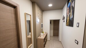 A hallway with a wooden door, a mirror, a console table with decorative items, a clock, and a painting on the wall. - Catania Center B&B (Catania)
