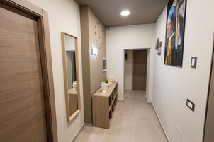Un pasillo con una puerta de madera, un espejo, una consola decorativa y un cuadro en la pared.