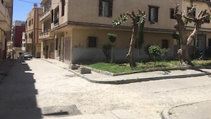 A multi-story building with a flat facade, several windows, and a small garden area with trees and shrubs. - Beautiful Apartment for those looking for Calm (Tanger)
