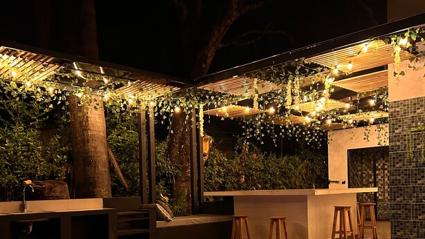 Ein Poolbereich im Freien mit Holzterrasse, einer Bar mit Hockstühlen und Lichterketten.