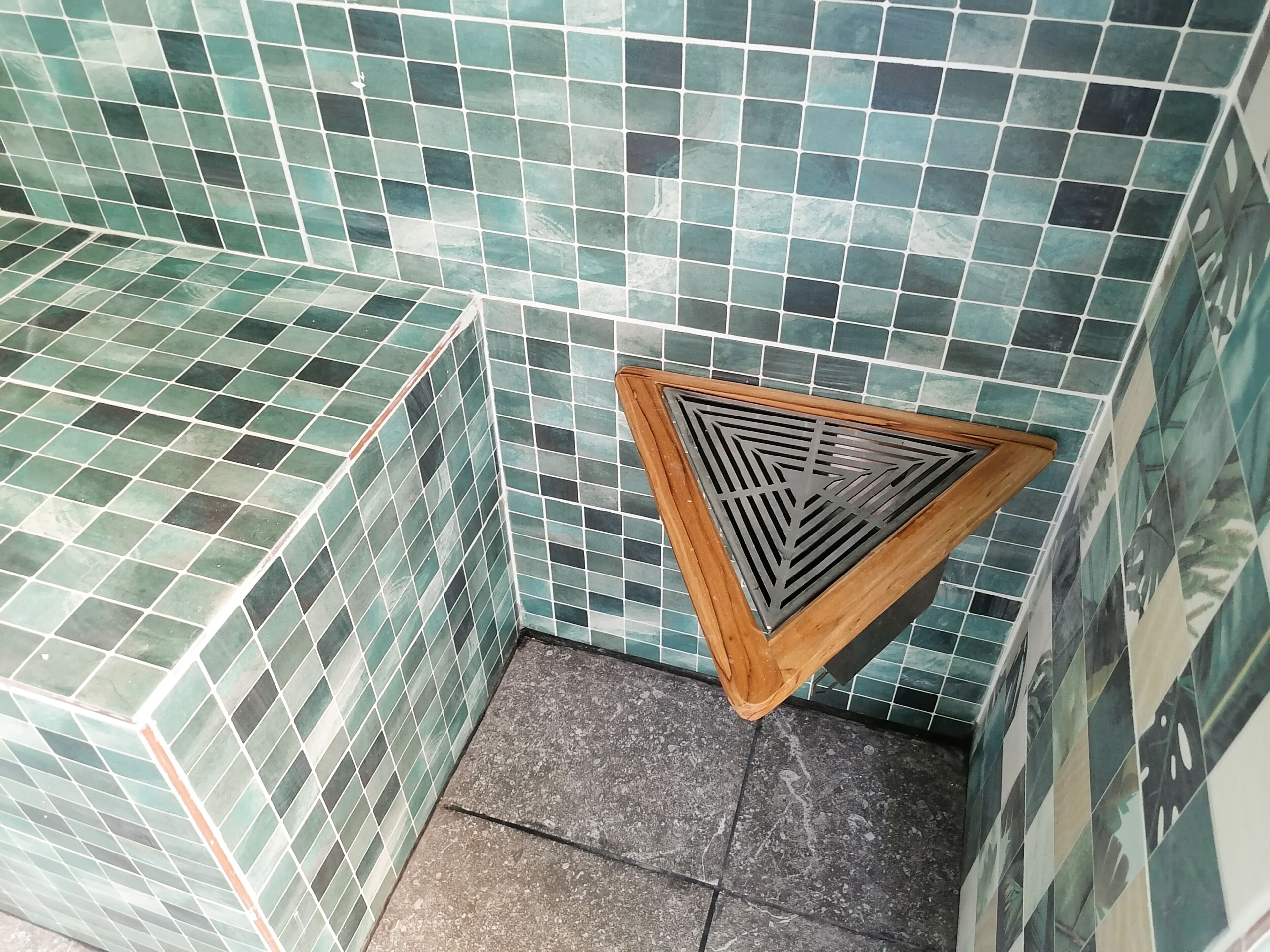 A corner of a room with green mosaic tiles on the walls and a wooden vent.