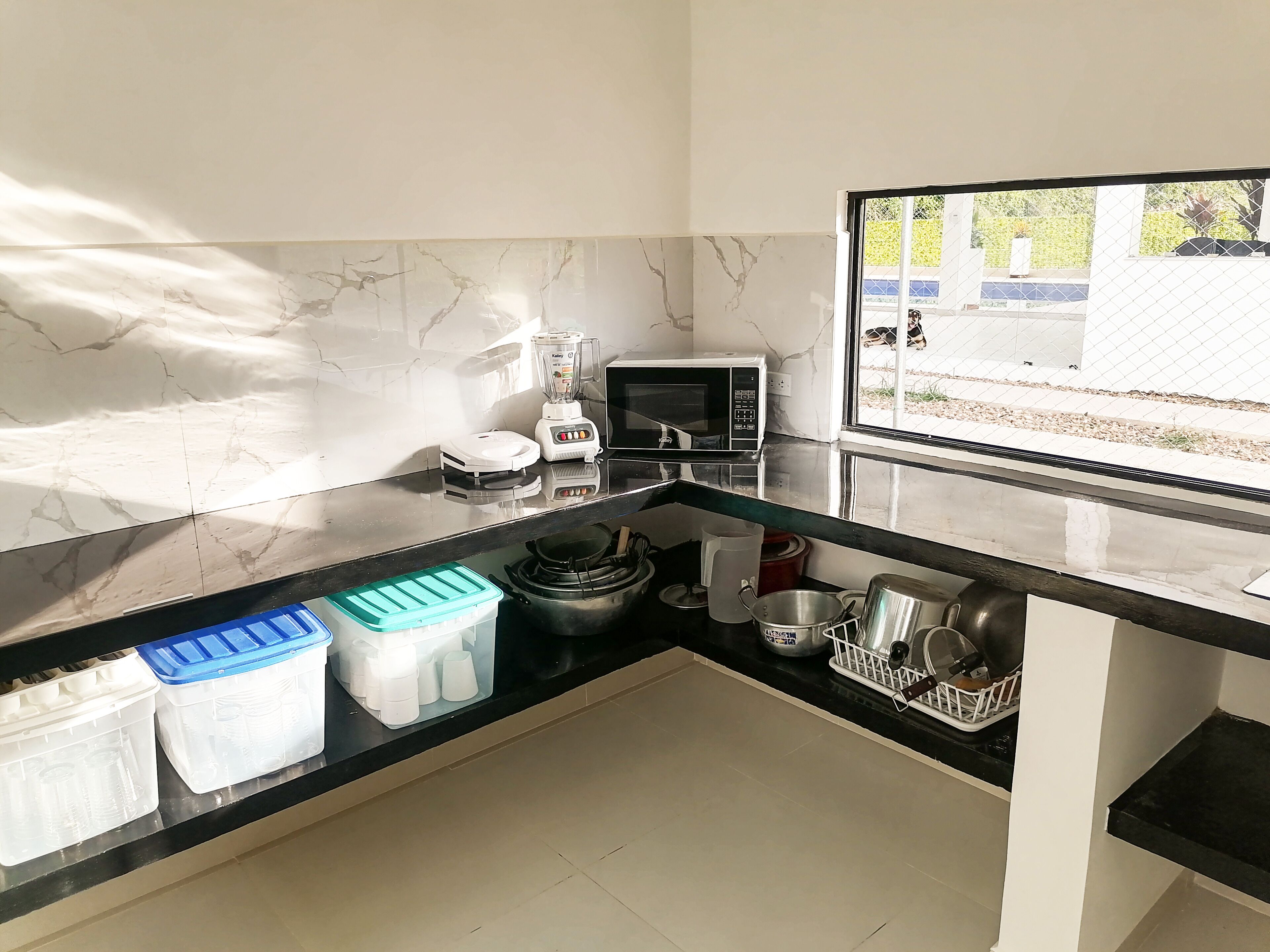 Una cocina moderna con encimera negra, salpicadero de mármol blanco y ventana con vistas a un jardín.