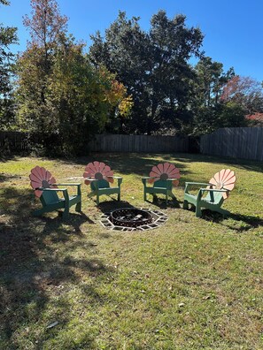 A backyard with a fire pit surrounded by green chairs and a table.