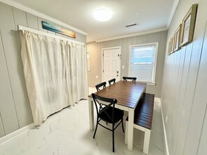 A dining area with a wooden table and chairs, a white curtain, a door, and a window with blinds.