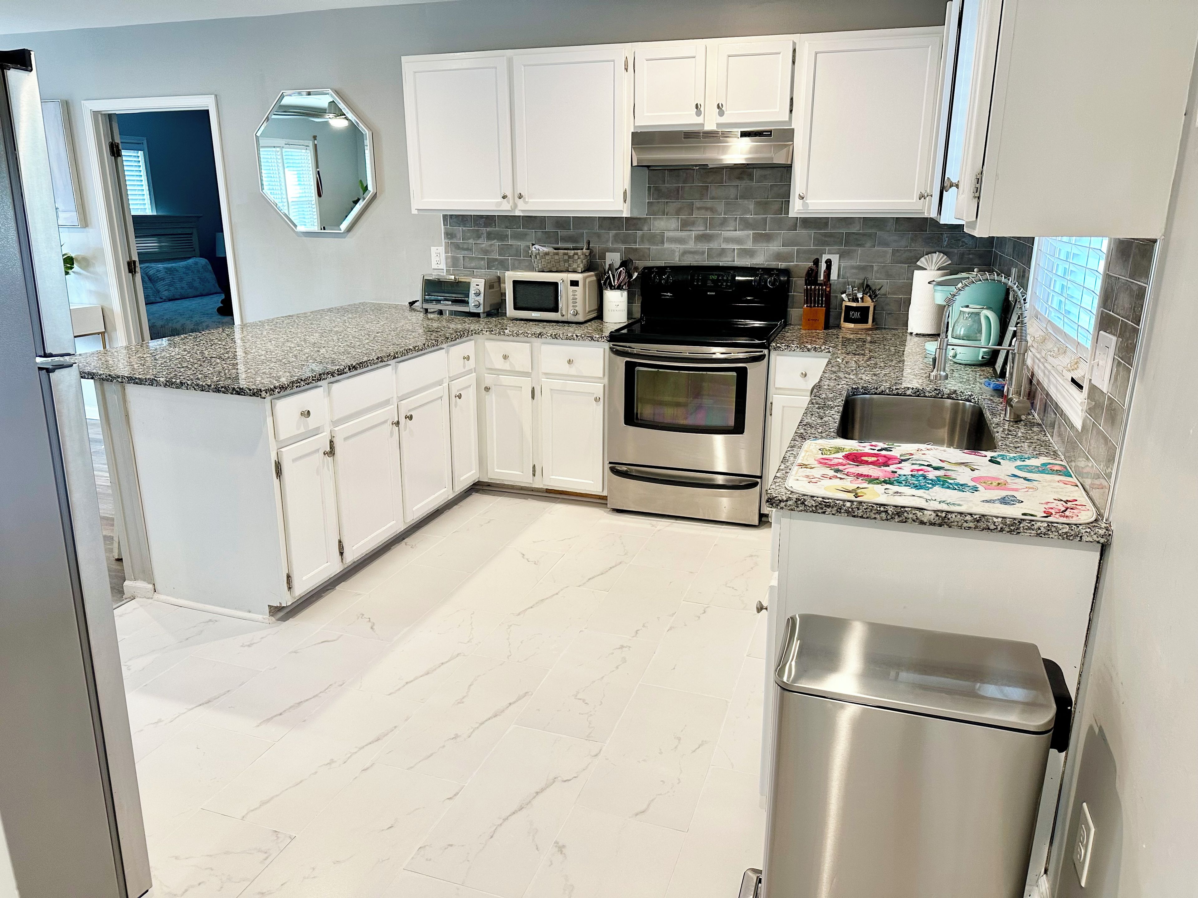 A modern kitchen with white cabinets, a stainless steel refrigerator, a microwave, an oven, and a sink.