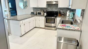 A modern kitchen with white cabinets, a stainless steel refrigerator, a microwave, an oven, and a sink.
