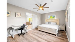 Ein Schlafzimmer mit Bett, Schreibtisch, Stuhl, Deckenventilator und Bildern an den Wänden.