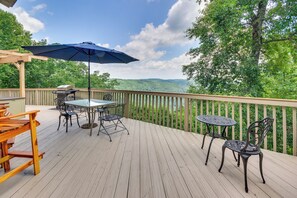 Eine Holzterrasse mit Tisch, Stühlen, einem Grill und einem blauen Sonnenschirm.