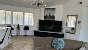 A spacious living room with a herringbone wood floor, a glass coffee table, a beige sofa, and a fireplace. - The Stylish Stay in Hesperia (Hesperia)