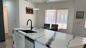 A modern kitchen with a marble countertop, a built-in dishwasher, and a window with blinds. - The Stylish Stay in Hesperia (Hesperia)