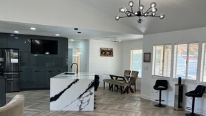 A spacious living area with a herringbone wood floor, a central island with a marble top, a dining area with a table and chairs, and a kitchen with dark cabinets and a built-in oven. - The Stylish Stay in Hesperia (Hesperia)
