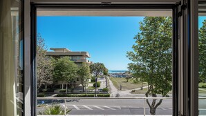 Une vue depuis une fenêtre donnant sur une rue, avec un bâtiment moderne, des arbres et un ciel dégagé.