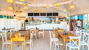 Un restaurant avec des tables et des chaises en bois, des lampes en osier suspendues et un coin bar.