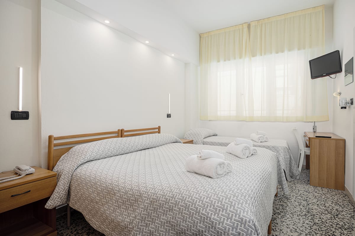 Habitación de hotel con una cama grande, una cama más pequeña, un escritorio, una silla, un televisor y una mesita de noche con un teléfono.