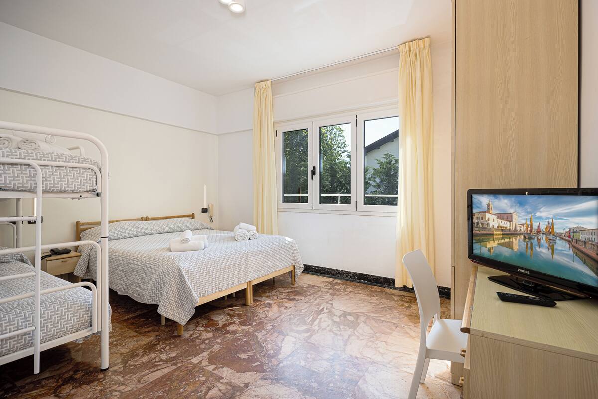 Una habitación de hotel con literas, un escritorio con televisor y una ventana con cortinas.