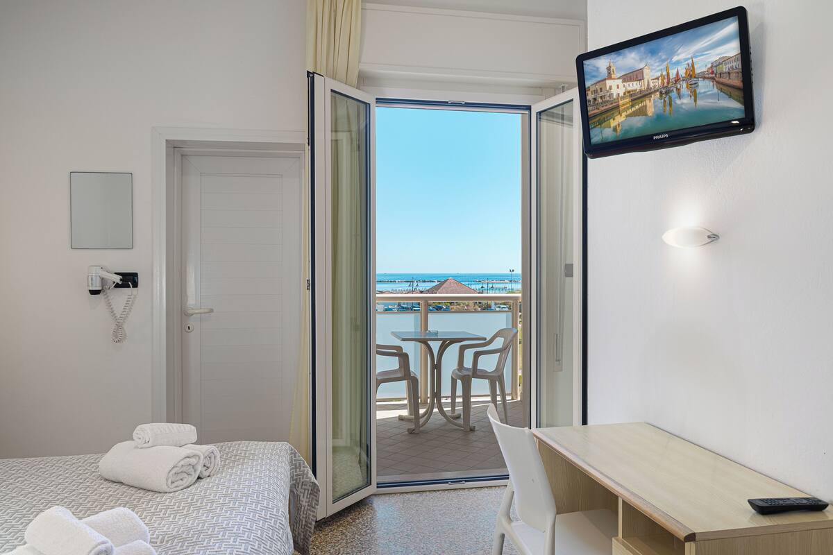 Habitación de hotel con cama, escritorio, televisión y balcón con vista al mar.