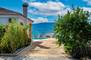 A pathway leading to a pool with a mountain view, surrounded by greenery and a white building with a tiled roof. - Villa Lomillas DE Canca Caminito del Rey (Alora)