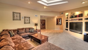 A living room with a sectional sofa, a coffee table, a TV, and a bookshelf. - Listing Description has Discounts! Kierland Home w/Pool & Hot Tub & Nearby Park! (Scottsdale)