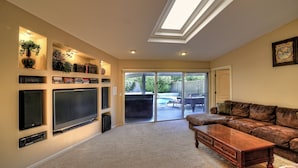 A living room with a large flat-screen TV, a leather couch, and a sliding glass door leading to a patio with outdoor furniture. - Listing Description has Discounts! Kierland Home w/Pool & Hot Tub & Nearby Park! (Scottsdale)