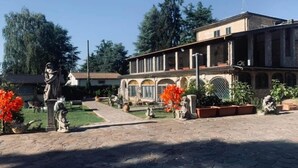 A courtyard with a building featuring arched windows and a tiled roof. There are statues and potted plants in the foreground. - Bed and Breakfast Simonelli RoomS (Rocca Priora)