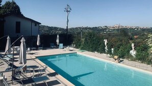 A swimming pool with lounge chairs and umbrellas, surrounded by a wooden deck and a view of a hillside town. - Bed and Breakfast Simonelli RoomS (Rocca Priora)