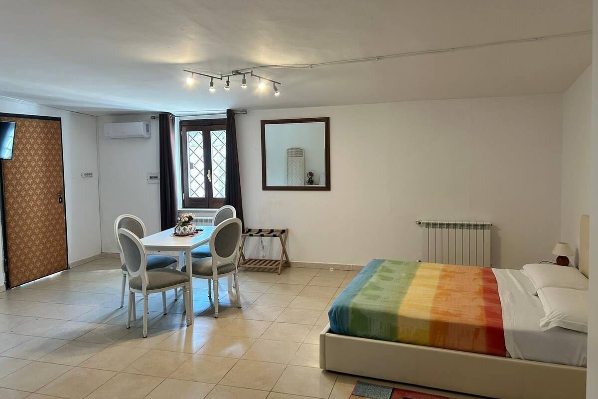 A room with a bed, a table with chairs, a window, a radiator, and a mirror on the wall.