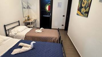 Habitación de hotel con dos camas, una mesita con una silla, una puerta decorada con un sol y un cartel en la pared.
