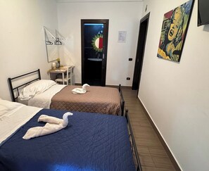 Una camera d'albergo con due letti, un tavolino con una sedia, una porta decorata con un motivo solare e un quadro appeso al muro.