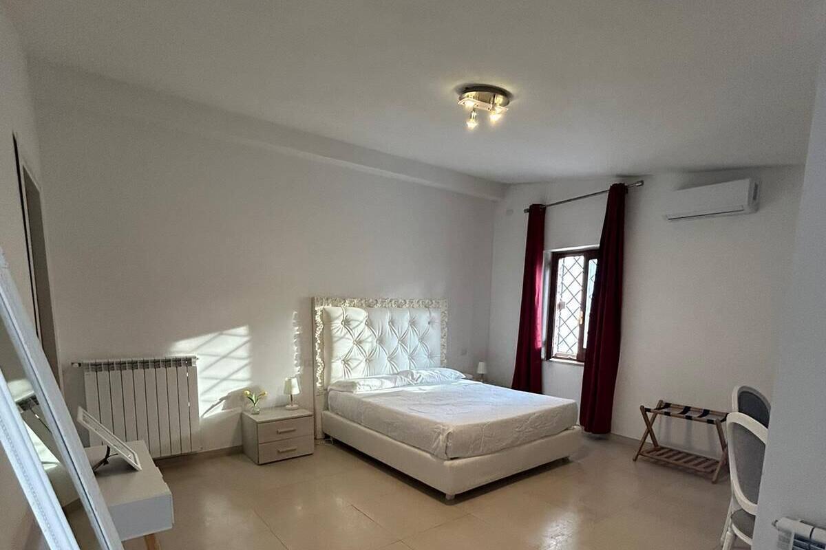 A spacious bedroom with a large bed, a bedside table, a radiator, and a window with curtains.
