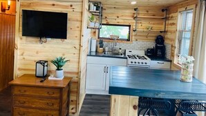 A compact kitchen with wooden walls, a flat-screen TV, a gas stove, and a coffee maker.