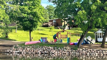 A lakeside property with a wooden play structure, a small shed, and a grassy area with a playground.