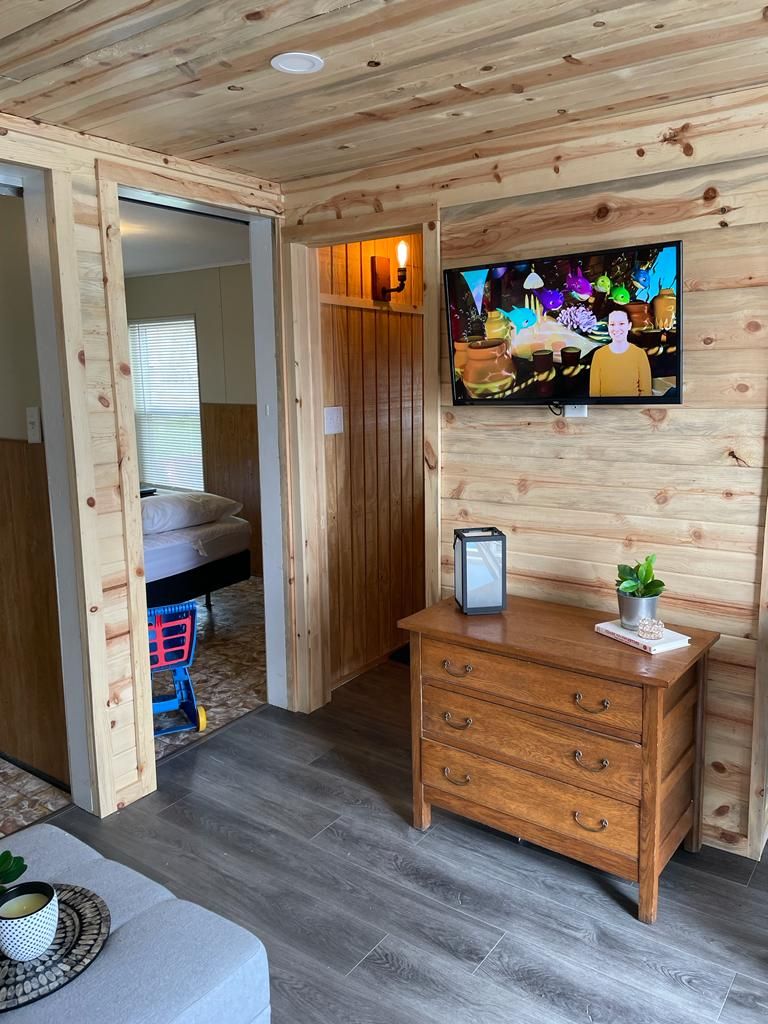 A room with a wooden ceiling, a television mounted on the wall, a wooden dresser, and a bed with a headboard.