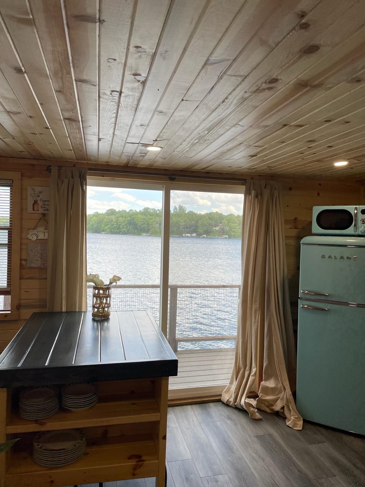 Una cabaña con interior de madera, una mesa de comedor, un refrigerador y vistas a un lago.