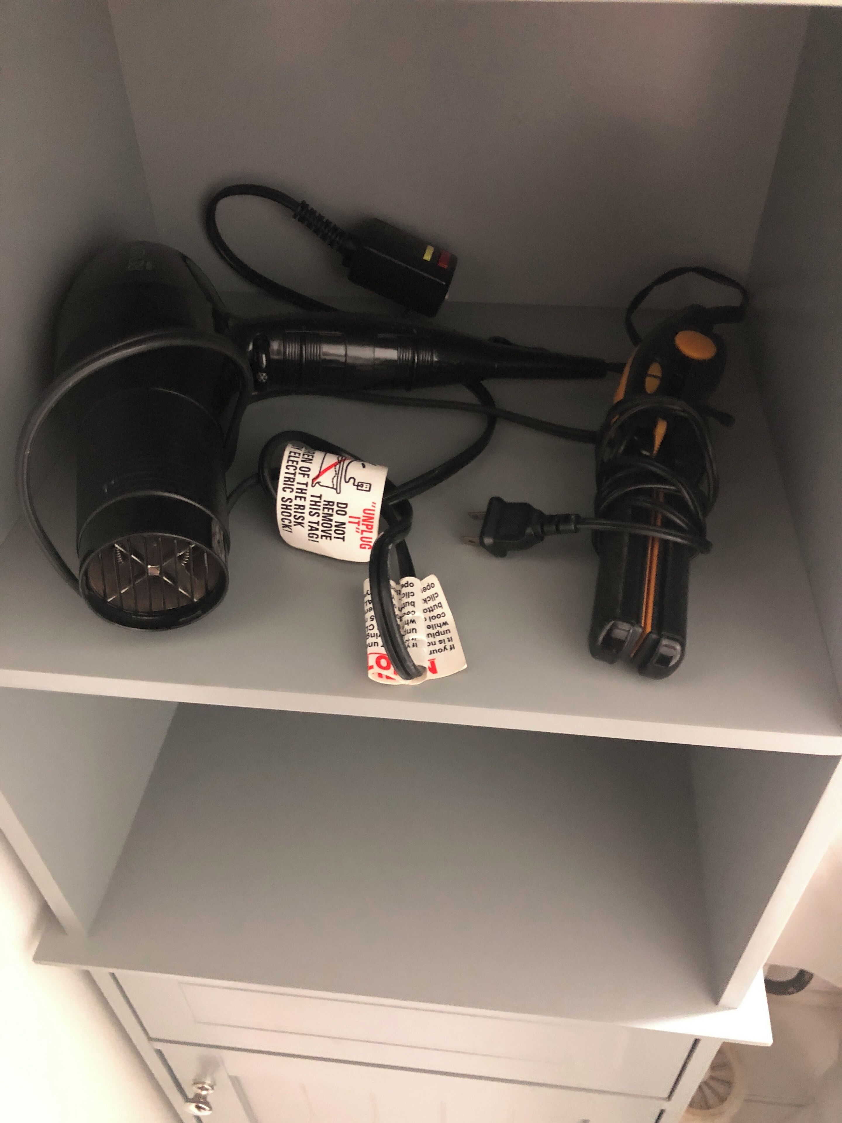 Une étagère avec un sèche-cheveux, un aspirateur et une multiprise.