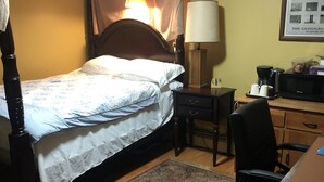 Ein Schlafzimmer mit einem Himmelbett, einem Schreibtisch mit Lampe, einem Sessel und einer Kaffeemaschine.