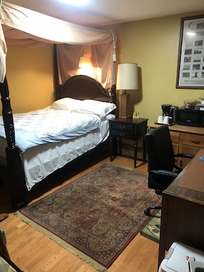 A bedroom with a four-poster bed, a desk with a lamp, a chair, and a coffee maker. - Bedroom with private full bathroom, linen and towels are provided. (Chicago)