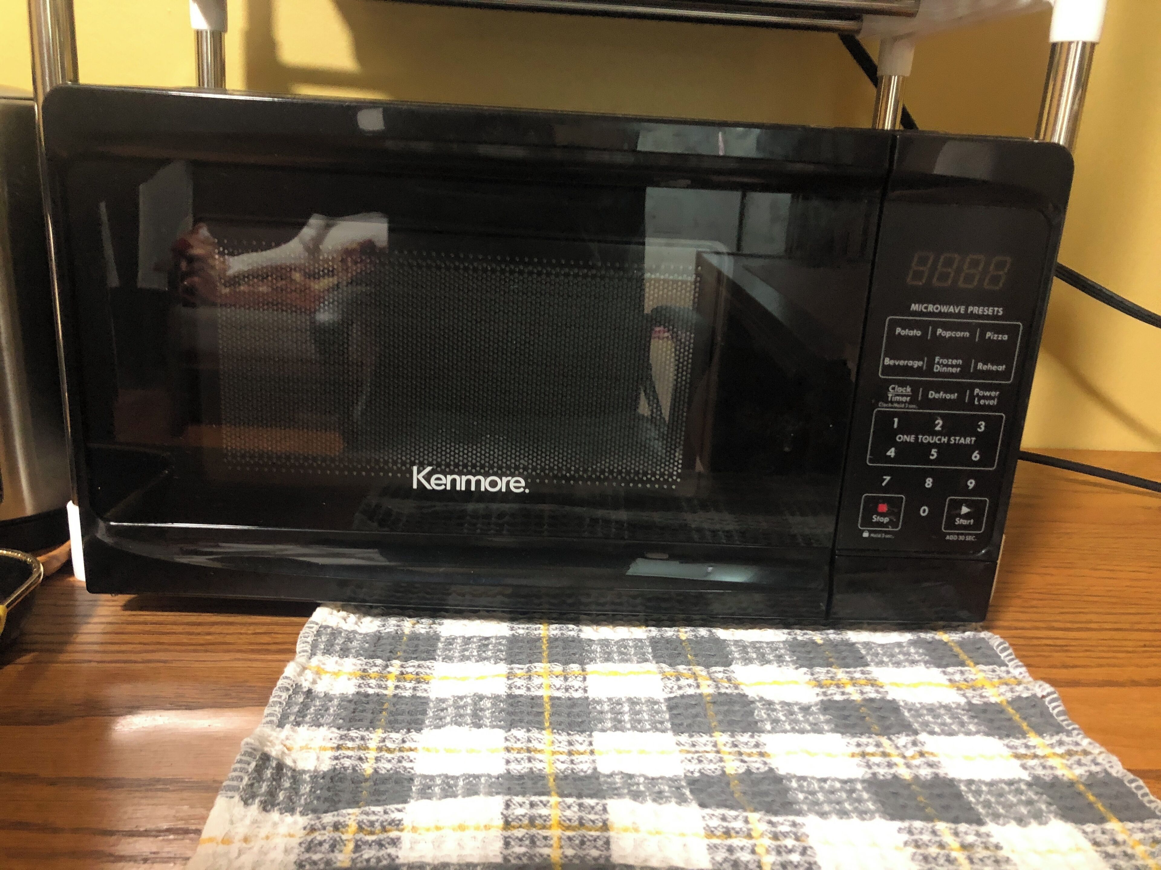 Een Kenmore magnetron op een houten tafel met een geruit tafelkleed.