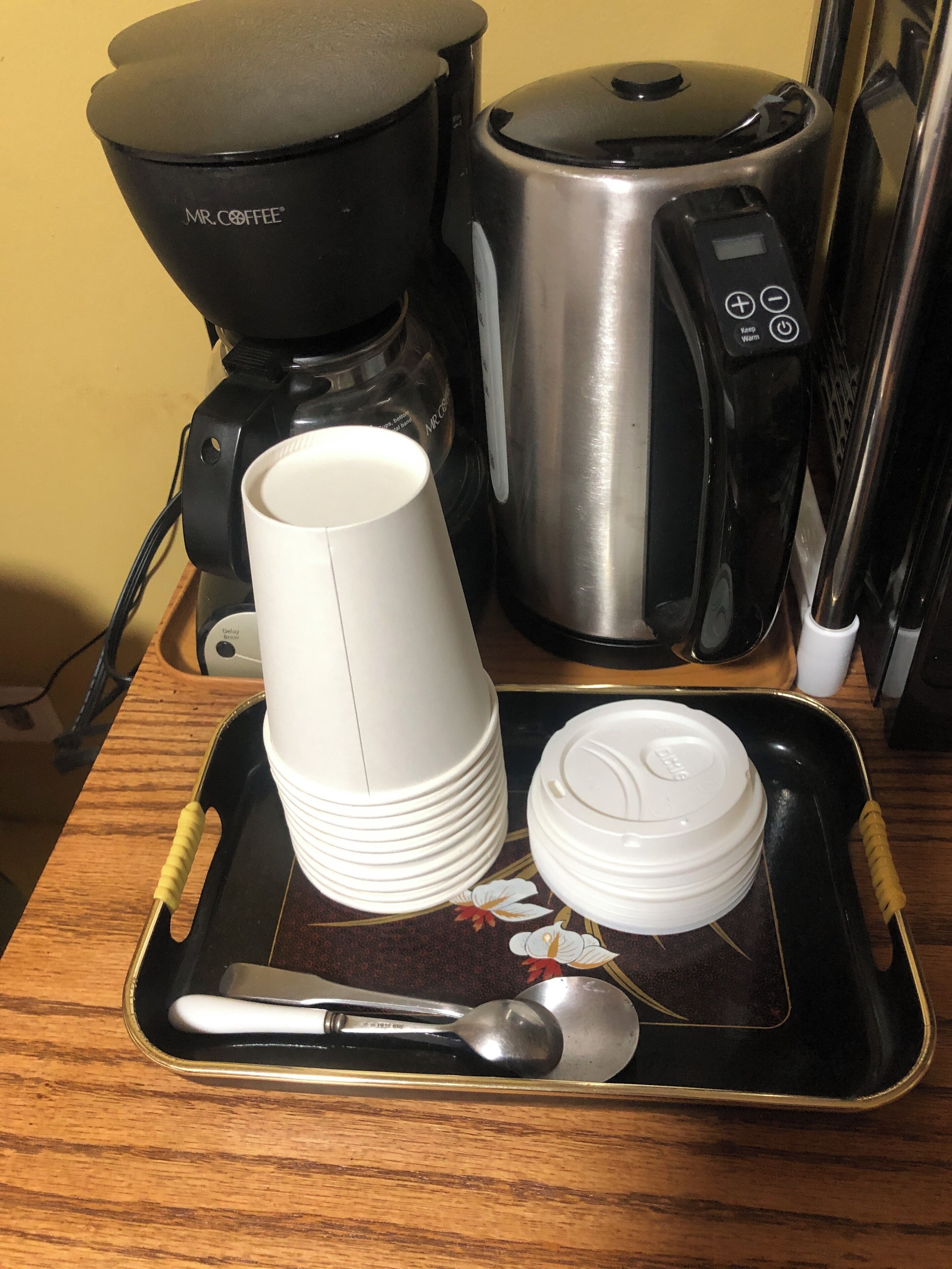 A tray with stacked white cups, a white cup, a white bowl, and a spoon on a wooden table.