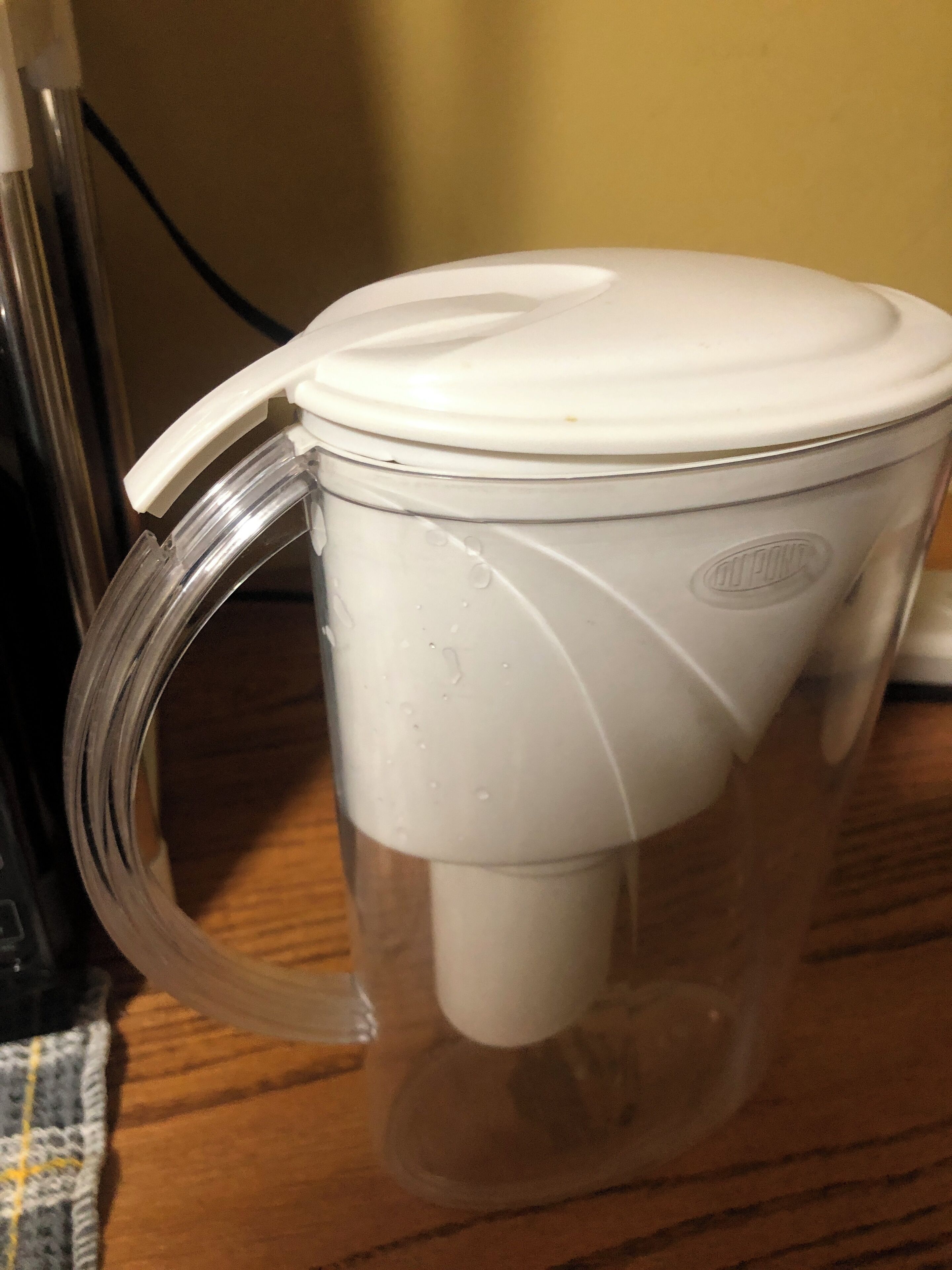 A clear glass mug with a white handle and lid, placed on a wooden surface.