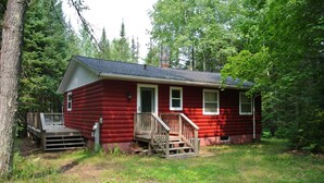 A red cabin with a wooden deck, surrounded by trees. - Tranquil Privacy (Rhinelander)