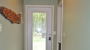 A hallway with a patterned rug, a door with a peephole, and a wall-mounted decoration. - Tranquil Privacy (Rhinelander)
