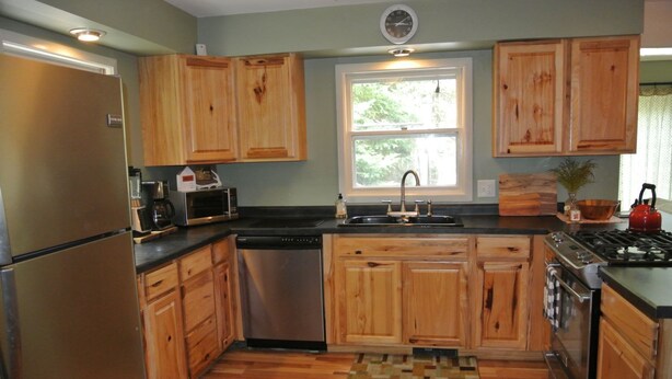 A kitchen with wooden cabinets, stainless steel appliances, a window, and a view of greenery outside. - Tranquil Privacy (Rhinelander)