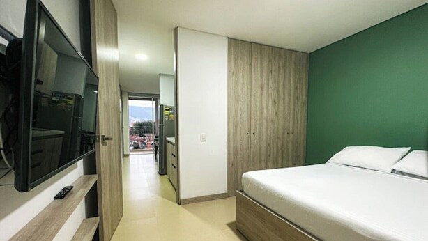 A modern hotel room with a large bed, a TV mounted on the wall, and a view of the outside. - Moderno y Acogedor Apartamento Medellín Laureles (Medellín)