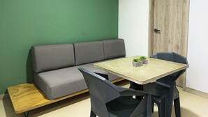 A room with a green wall, a grey sofa, a wooden bench, a table with two chairs, and a door with a wooden frame. - Moderno y Acogedor Apartamento Medellín Laureles (Medellín)