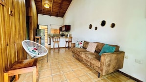 A cozy living room with a sofa, a chair, and a kitchen area in the background. - Beautiful & Cozy Casa Aire, Near Lake Arenal (Nuevo Arenal)