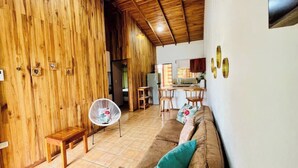 A cozy living area with a wooden wall, a sofa, a small table, and a fan. - Beautiful & Cozy Casa Aire, Near Lake Arenal (Nuevo Arenal)