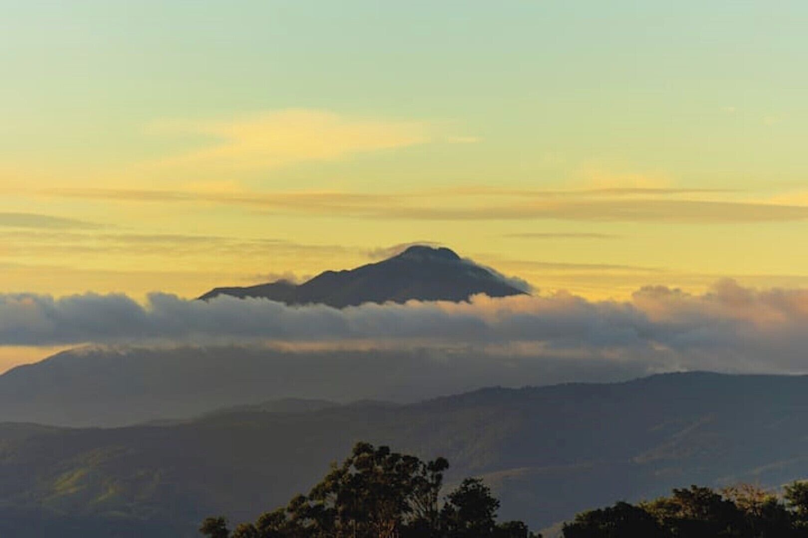 A mountain with a peak, surrounded by clouds and lower hills.