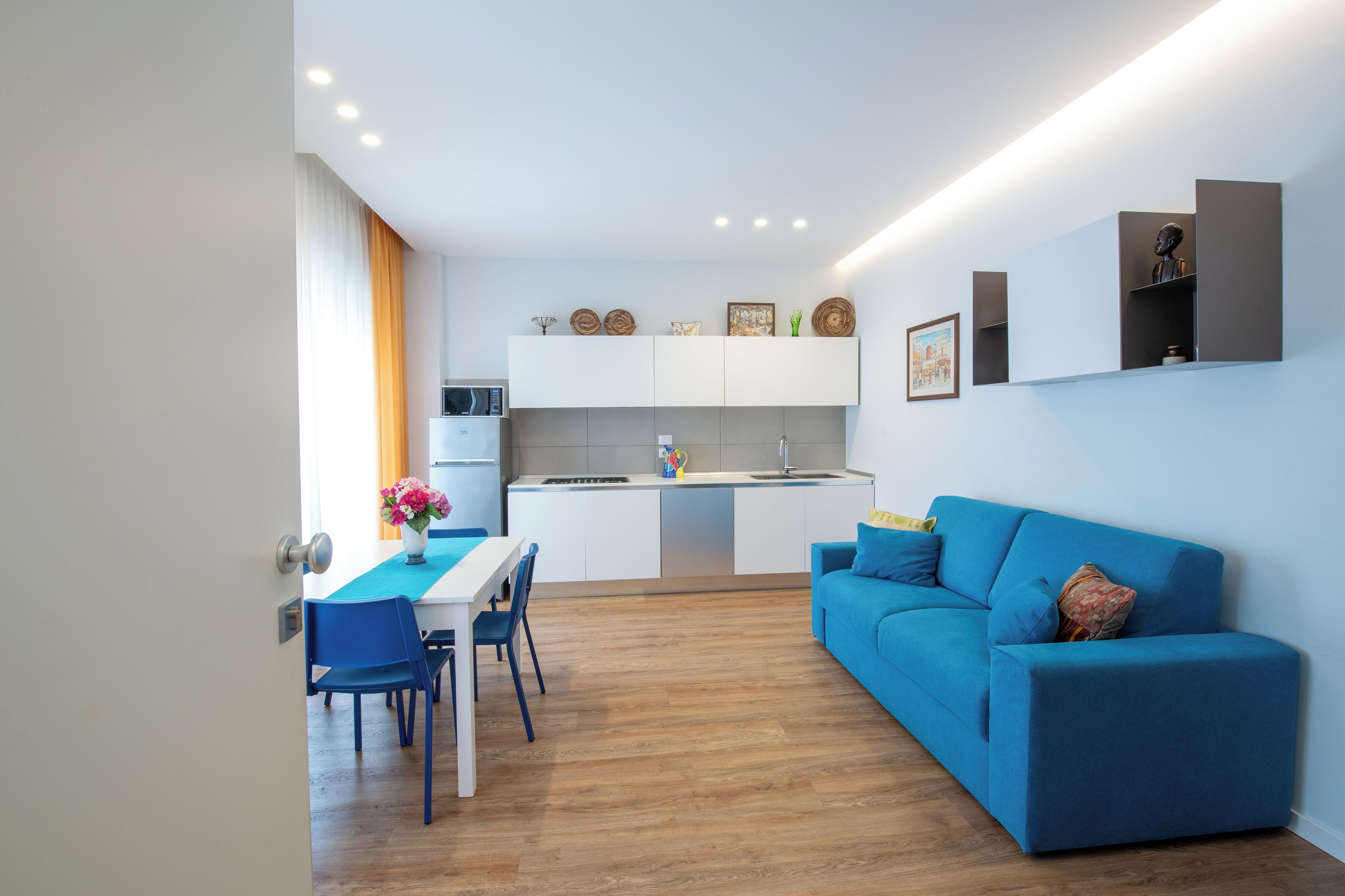 Una cocina moderna con armarios blancos, una mesa de comedor con sillas y un sofá azul.