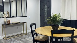 A dining area with a round wooden table, black chairs, a console table with decorative items, a potted plant, and a dark wooden door. - Your Forever Home (Lutz)